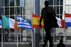 A pedestrian walks towards the Irish, Greek, Spanish, French and Dutch national flags outside the European Parliament in Brussels