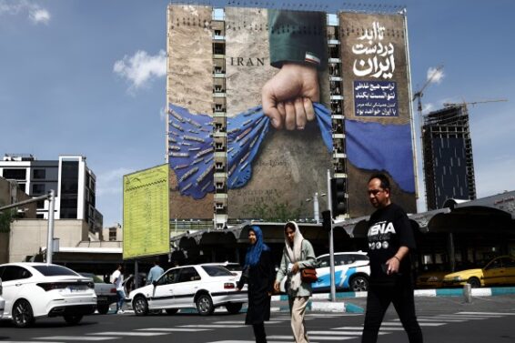 People walk past a billboard with a graphic design about the Strait of Hormuz on a building